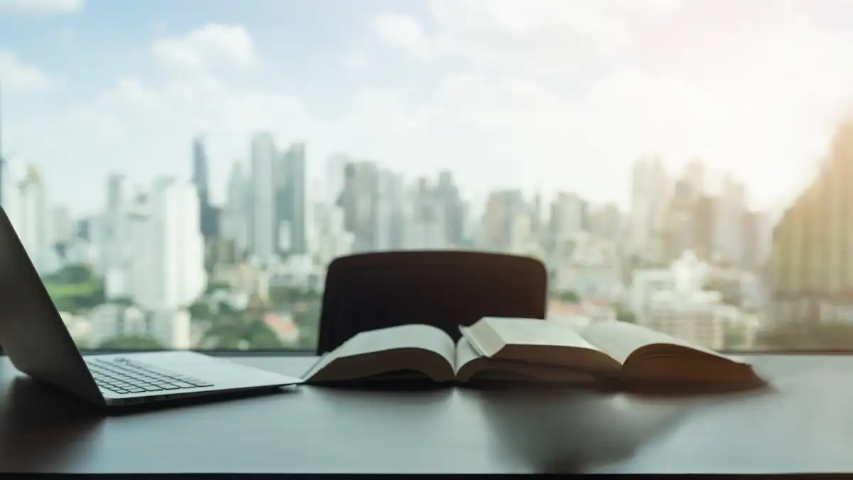 Ambiente de trabalho com laptop e livros abertos, com vista panorâmica para uma cidade